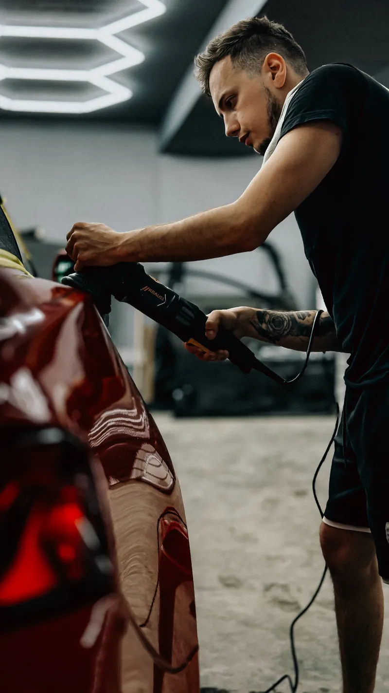 Professionnel réalisant une finition sur une carrosserie rouge, illustration d’ambiance